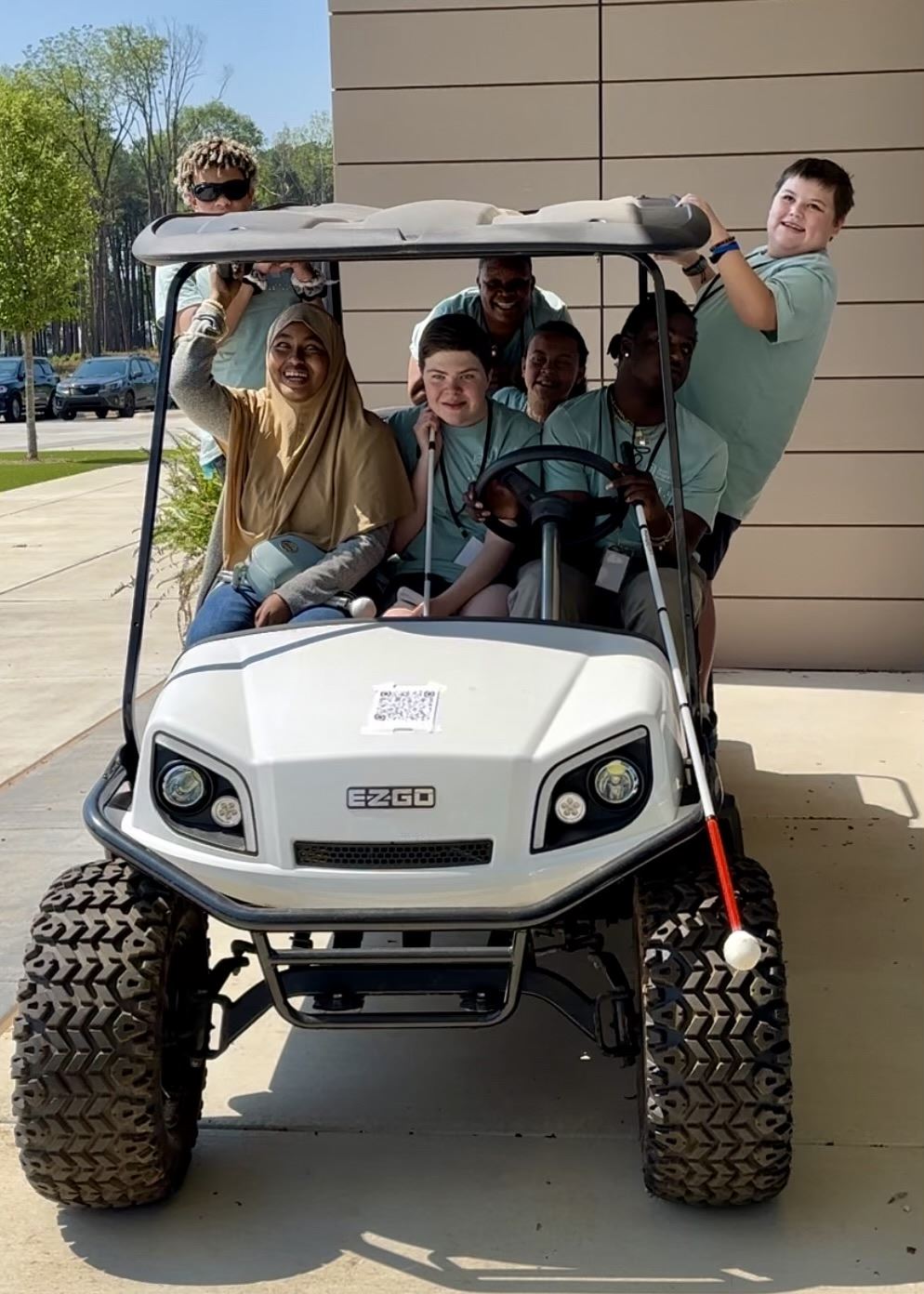 Group of high school students in a golf cart pretending to drive. The driver has her white cane hanging out the front window. Group of high school students in a golf cart pretending to drive. The driver has her white cane hanging out the front window.